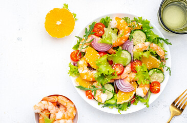 Fresh shrimp salad with orange, lettuce, tomatoes, cucumbers, onions and sesame seeds with olive oil, white background, top view