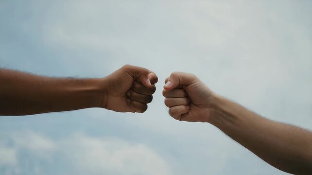 A friendly fist bump between two diverse individuals, symbolizing unity, partnership, and mutual respect against a blue sky background.