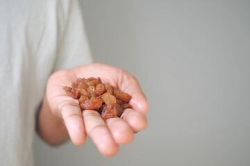 Hand holding dried raisins on neutral background