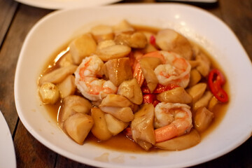 stir fried shiitake mushroom and shrimp with soy sauce in a ceramic dish on wooden table, close up. homemade style food concept.