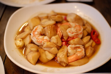 stir fried shiitake mushroom and shrimp with soy sauce in a ceramic dish on wooden table, close up. homemade style food concept.