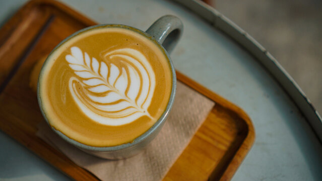 A close-up view of a cup of coffee with intricate latte art in the shape of a leaf