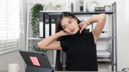 Fototapeta premium A woman is stretching her neck while sitting at a desk with a laptop
