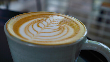 A close-up view of a cup of coffee with intricate latte art in the shape of a leaf