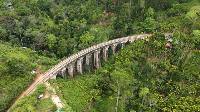 Aerial 4K drone footage of the iconic Nine Arch Bridge near Ella, Sri Lanka. Stunning views of the historic railway viaduct, lush green hills, and scenic train crossing for travel and tourism projects