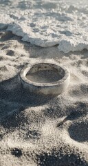 A pale, round object rests in the sand at the edge of a foamy ocean