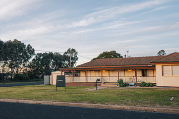For sale sign in front yard of large weatherboard home on corner of quiet street