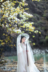 Young woman in traditional dress by riverside with spring flowers.