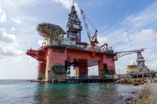 Plataforma de petr&oacute;leo offshore em Cura&ccedil;ao, vista de perto no porto, destacando estrutura industrial, guindastes e opera&ccedil;&atilde;o mar&iacute;tima sob c&eacute;u parcialmente nublado.
