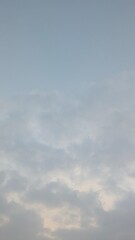 A calm, vertical shot of a cloudy sky at dawn. The light-colored clouds are concentrated at the...