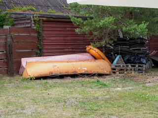 An old weathered wooden boat, possibly for fishing, lies on the grass next to a rustic shed in a...