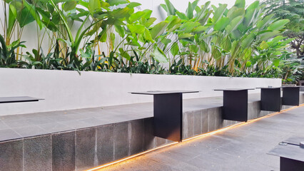 Cozy modern outdoor cefe with black metal table, lush tropical plants in white pot, and urban building backdrop. Perfect for relaxaxing and enjoying coffee. peacefull ambient.