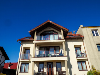 A multi-story traditional European building with balconies and a red roof under a bright blue sky on a sunny day.