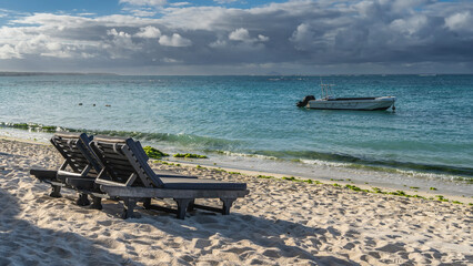Two deck chairs with mattresses on the sandy beach. Foam waves and green algae on the sand. A...