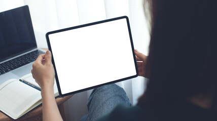 Mockup image of woman using digital tablet with blank white screen during working with laptop...