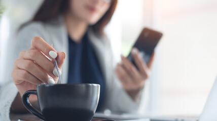 Business woman using mobile phone during working on laptop computer, hand holding a cup of coffee on office table, closeup, people lifestyle, taking a coffee break