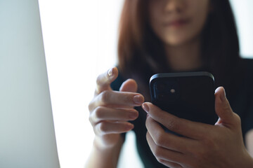 Closeup, happy business woman using mobile phone during working on laptop computer at coffee shop. Young asian freelancer, entrepreneur using smartphone, online working at home office