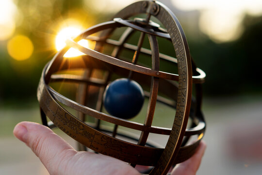 Close-up of vintage armillary globe against golden sunset. Armillary sphere on hand, spherical astrolabe. Medieval astronomy astrology abstract concept symbol