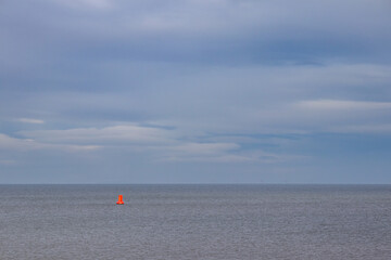 Vibrant red buoy positioned in open water, contrasting with the muted tones of the calm sea and...