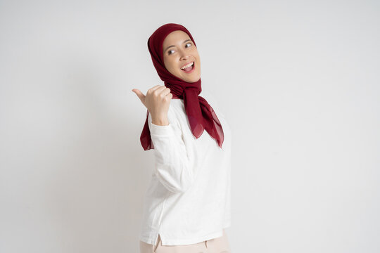 Young woman wearing a red hijab and white top expressing surprise while pointing sideways. Studio shot against a white background, highlighting emotions, cultural attire, and a moment of astonishment. - Powered by Adobe