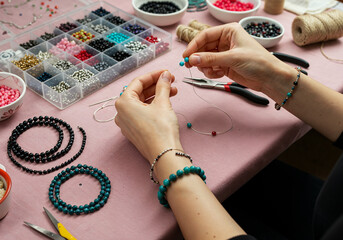 Top View of Female Hands Crafting Jewelry with Colorful Beads and Tools on a Pink Table