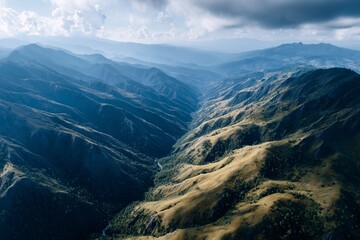 Obraz premium Aerial view of green valleys and ridges stretching into distance under cloudy sky with sunlight casting shadows