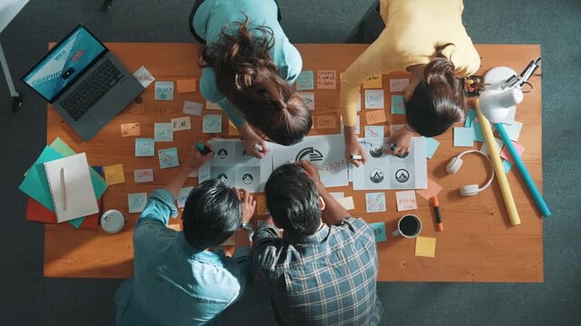 Time lapse of business team put graphic logo on meeting table with colorful sticky notes and start to design while explain idea. Project manager walking at group while explain concept art. Symposium.