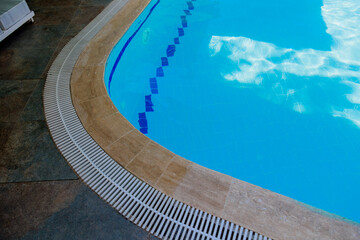 Top view of a blue water outdoor swimming pool with brown tiles around its edges. Vertical close-up...