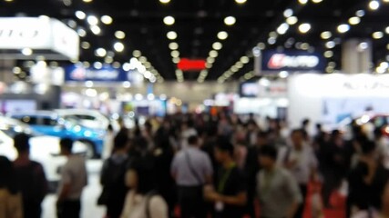 Blurred crowd at an auto show with cars and booths visible in the background