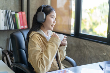 A woman wearing headphones is sitting at a desk with a cup of coffee