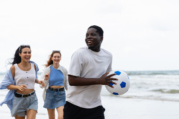 Young people enjoy summer outdoor activities on beach with friends playing ball and running happily along shore creating joyful moments by sea