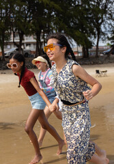 Three young people enjoy summer outdoor activities on beach with people holding hands running...