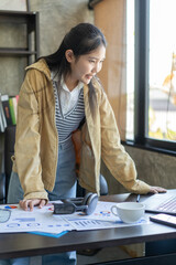 A woman wearing a yellow jacket is standing in front of a desk with a laptop