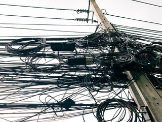 Messy tangled overhead cable wires on utility pole in urban city infrastructure.