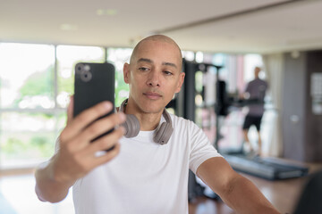 Latin man cycling on stationary exercise bike in gym while using mobile phone
