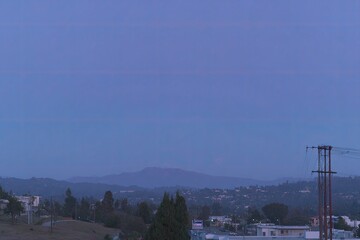 Pale lavender sky, moon over distant hills, city below