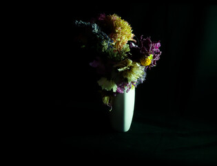 High contrast photograph of dried flowers in white vase. Black background against coloured flowers creates drama and gives space for text or graphics.