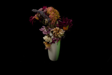 Floral arrangement of dried flowers in white vase. Black background against coloured flowers gives space for text or graphics.