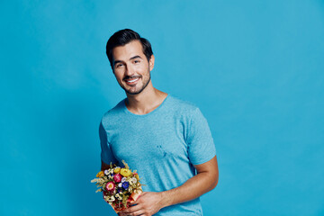 Cheerful smiling young man holding a colorful bouquet of flowers, wearing a casual blue t-shirt,...