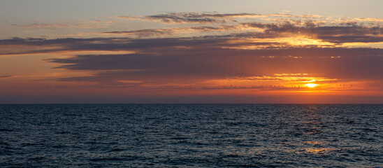 The sky is a beautiful orange color as the sun sets over the ocean