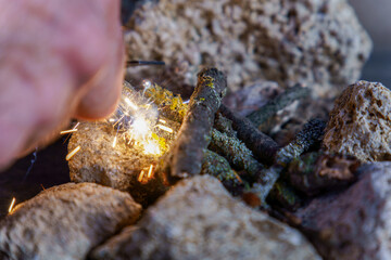 Hand striking magnesium rod to ignite tinder and start campfire in survival situation