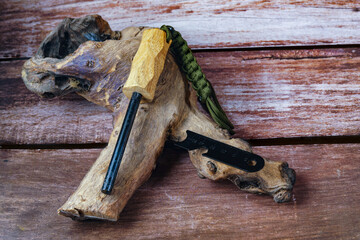 Ferrocerium rod with wooden handle, striker and paracord lanyard laying on a piece of wood and wooden background, ready for fire starting