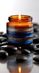 Amber candle in a recycled glass jar,  blue and teal stripes, surrounded by dark stones