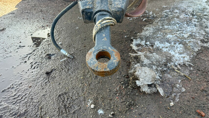 Rusty, heavy-duty metal hitch, agricultural equipment part lying on wet, muddy ground with melting...