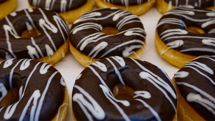 Chocolate glazed donuts with white icing drizzle, close-up dessert background