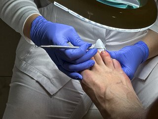 A podiatrist in a white coat and blue medical gloves performs a man's pedicure at a beauty salon....