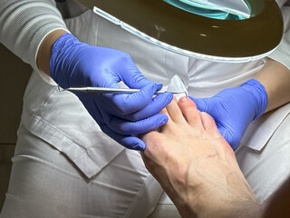 A podiatrist in a white coat and blue medical gloves performs a man's pedicure at a beauty salon....