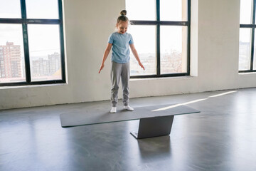 Child practicing balance on a mat in a bright room during a training session