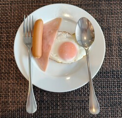 Fried eggs, ham, sausage on a white plate. Breakfast for you.