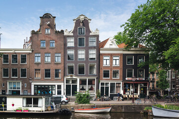 Charming Canal Houses and Boats Along a Picturesque Amsterdam Waterway with Lush Greenery and Clear Blue Skies